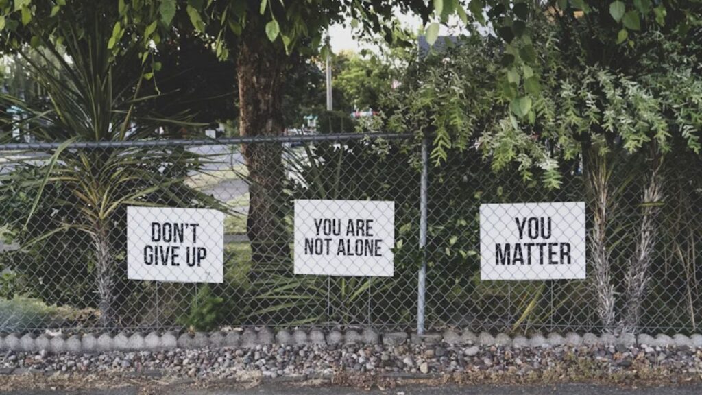 Signs behind chicken wire read “You Are Not Alone” in black block letters on a plain white background.