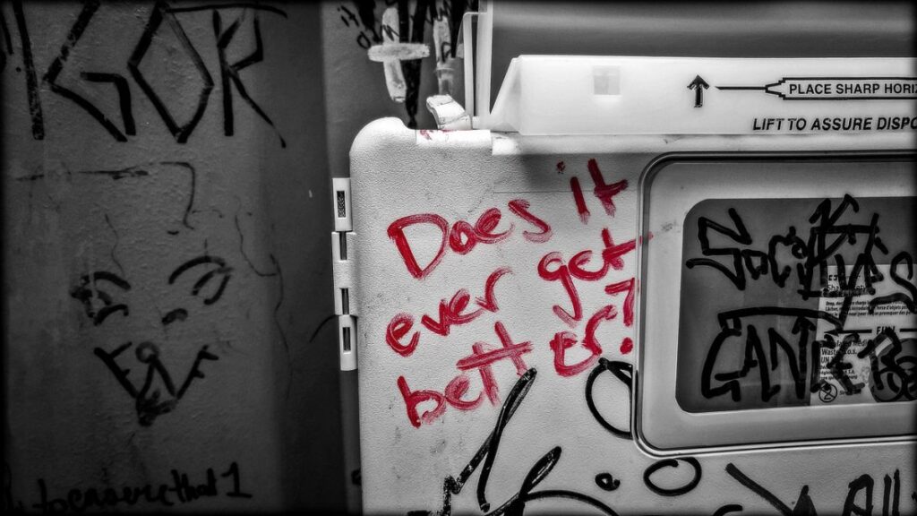 Red marker graffiti on a wall reads, “Does it ever get better?”