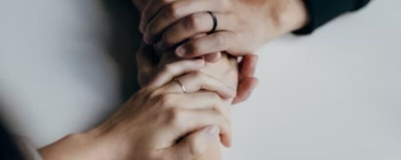 Three hands joined together on a white table, symbolizing trust, unity, and commitment.