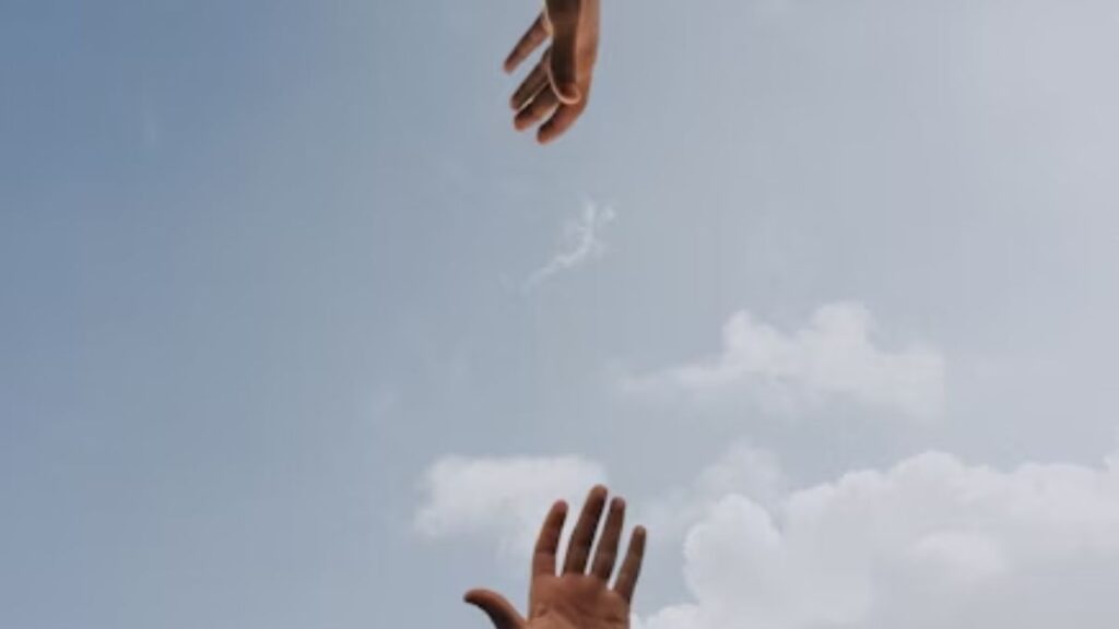 Two hands reaching out toward each other against a clear blue sky.