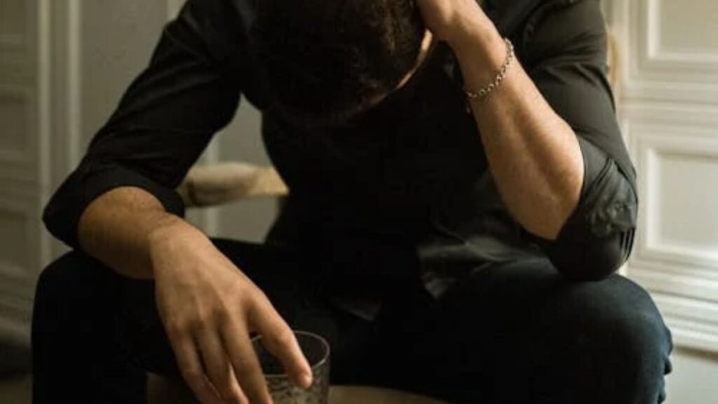 Man looking down, holding a drink, appearing lonely and dejected.