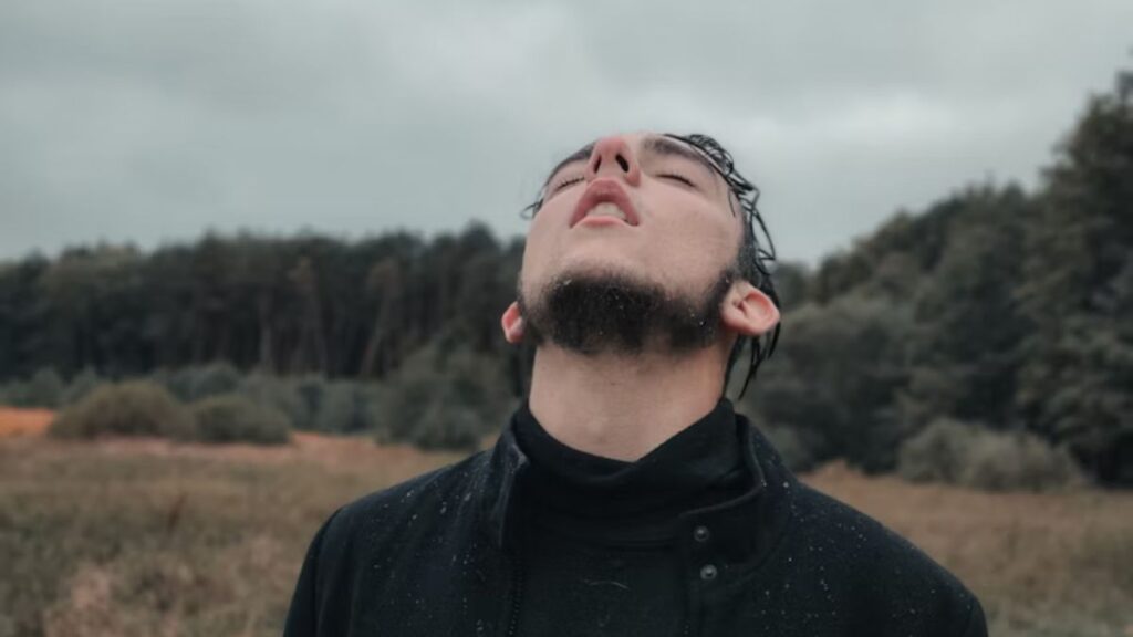 Man in pain looking upward in a wide open space beneath a vast sky.