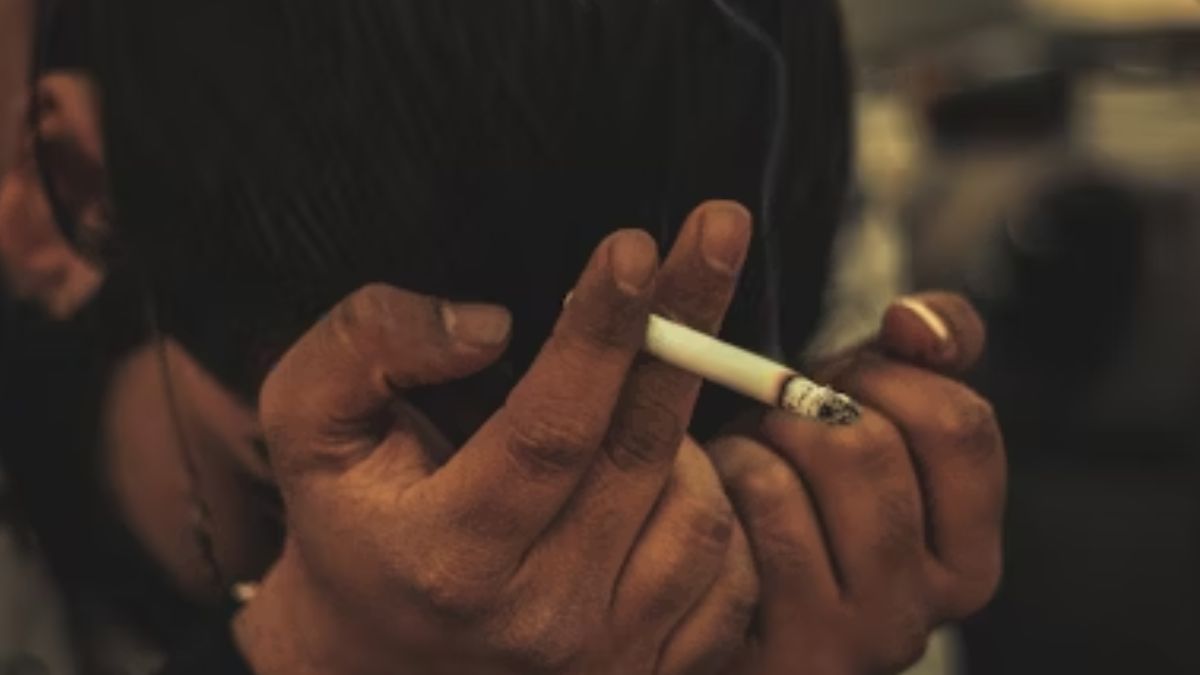 A man holds a cigarette with his face buried in his hands, appearing tired, disturbed, and trapped.