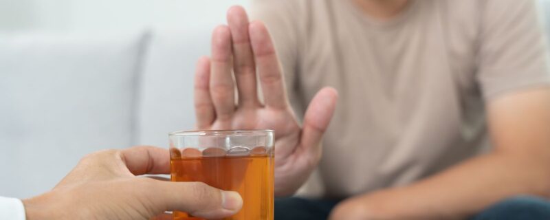 The hands of patients gently stop an offered hard liquor drink. The image is softly focused, showing only the hands.