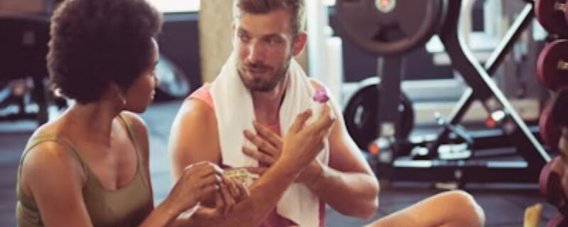 A man talks with his therapist and instructor in the midst of a busy gym.